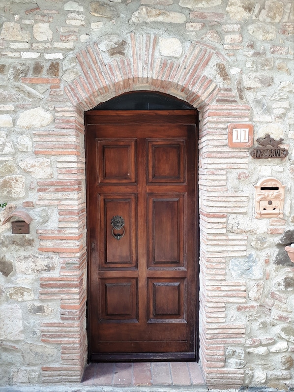 A wooden door with a metal knocker, set in a stone wall with a brick archway. - Toskanisches Natursteinhaus im Herzen der Maremma nur 20 Minuten vom Meer (Tuscany)