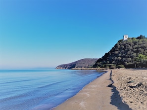 A beach with a clear blue sea, a sandy shore, and a hill with a building on top. - Toskanisches Natursteinhaus im Herzen der Maremma nur 20 Minuten vom Meer (Tuscany)