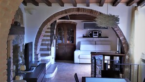 Un intérieur agrémenté d’une arche en briques donnant sur un espace de vie comprenant un canapé blanc, un téléviseur et une cheminée.