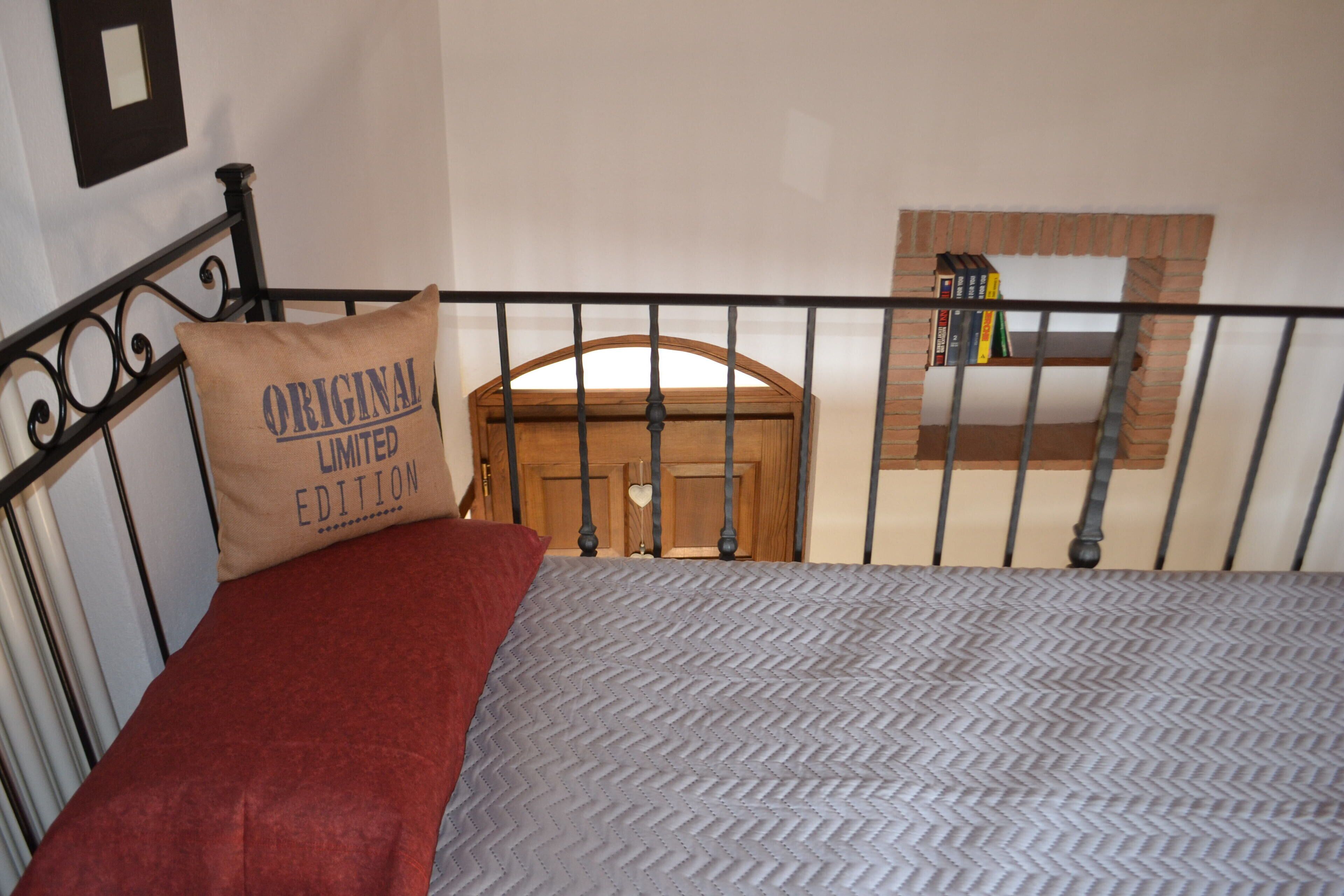 A bed with a patterned bedspread, a pillow with text, a red blanket, and a wooden headboard.