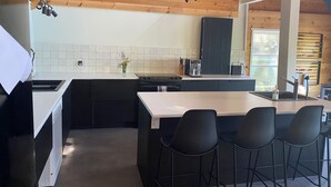 Een moderne keuken met een houten plafond, een centraal eiland met barkrukken, een inbouwoven en een zwarte afzuigkap.