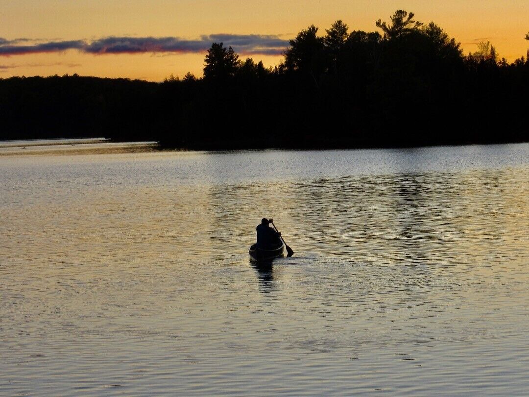 Una persona rema en un lago tranquilo al atardecer.