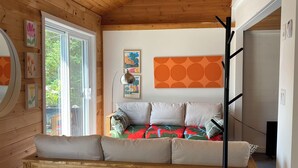 Een gezellige kamer met een houten plafond, een bed met kleurrijk beddengoed, een bankje en een groot raam.