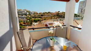 A balcony with a table, a potted plant, and a glass of orange juice. - Balcón del Golf - Riviera Cozy Apartment (Mijas Costa)