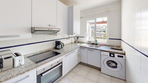 A compact kitchen with a built-in oven, a coffee maker, a washing machine, and a window with a city view. - Balcón del Golf - Riviera Cozy Apartment (Mijas Costa)