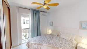 A bedroom with a bed, a ceiling fan, a window with curtains, and an air conditioning unit. - Balcón del Golf - Riviera Cozy Apartment (Mijas Costa)