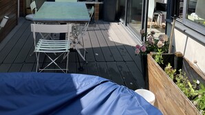 A patio with a table and chairs, a barbecue grill, and a window overlooking a garden.
