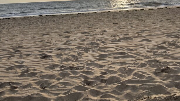 A beach with sand ripples and a sunset in the background.