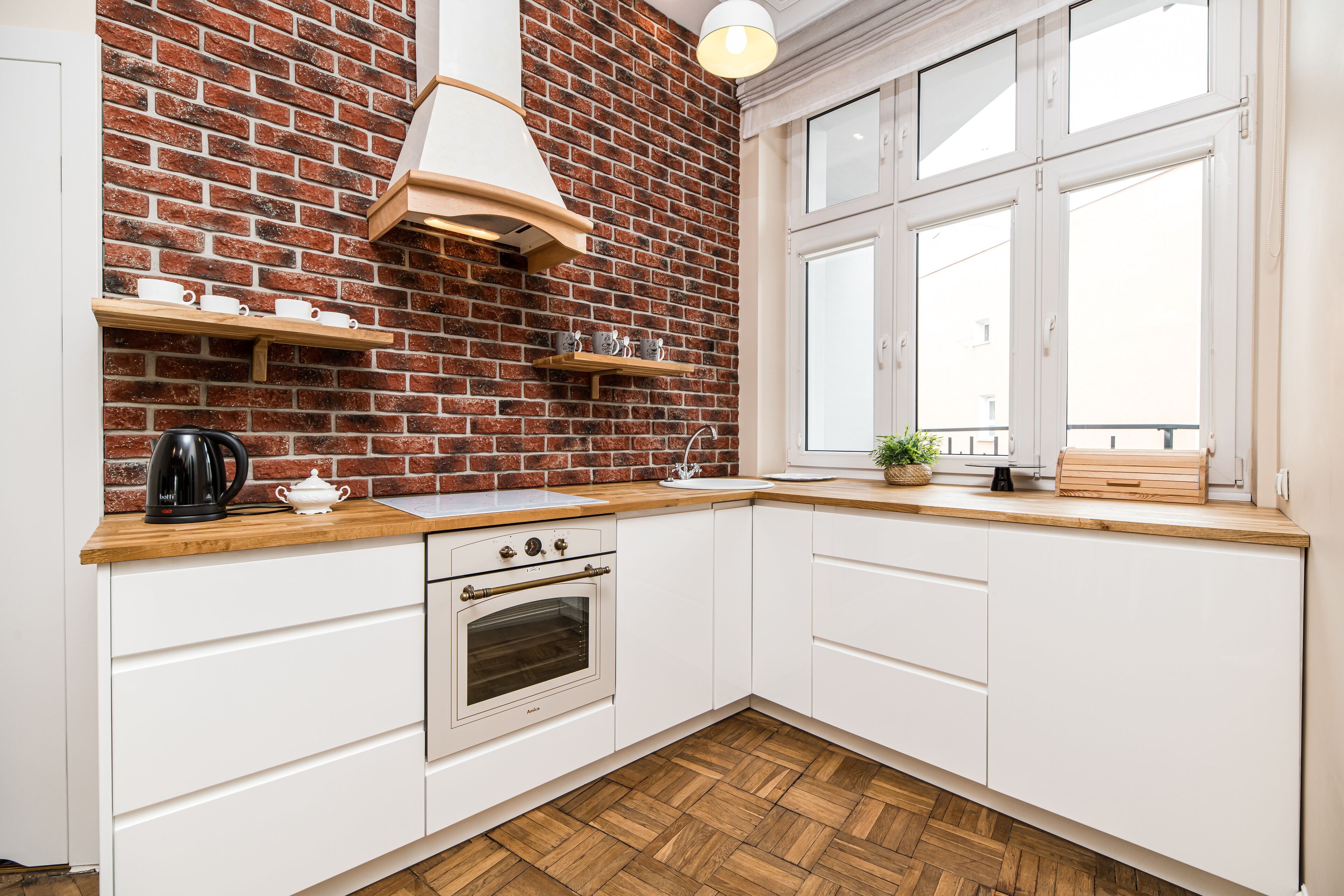 A kitchen with white cabinets, a brick wall, a wooden countertop, a stove, and a window with a view. - Native Apartments Batorego 7 (Kraków)