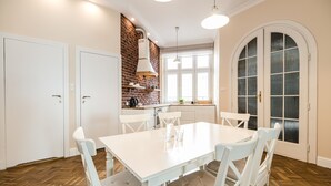 A dining area with a white table and chairs, a brick accent wall, and a large arched window. - Native Apartments Batorego 7 (Kraków)
