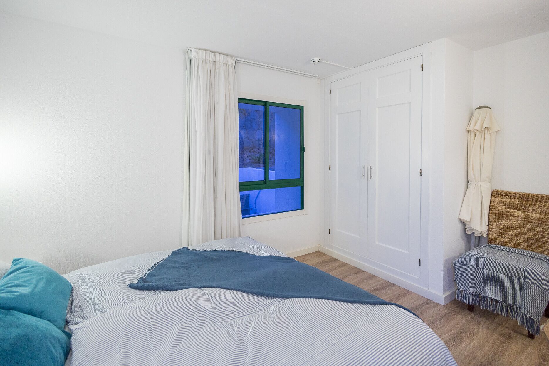 A bedroom with a bed, a window, a wardrobe, and a small bench.