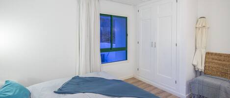 A bedroom with a bed, a window, a wardrobe, and a small bench.