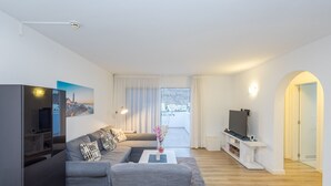 A modern living room with a sofa set, a flat-screen TV, and a balcony with a view. - 2BR Private Terrace House-Solarium & Pool (Mogán)