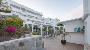 A modern outdoor seating area with stone walls, a pergola, and a staircase leading to a white building. - 2BR Private Terrace House-Solarium & Pool (Mogán)