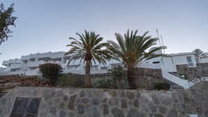 A coastal building with a stone wall, palm trees, and a staircase leading to upper floors. - 2BR Private Terrace House-Solarium & Pool (Mogán)