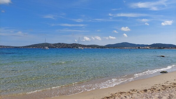 A beach with clear water, a sandy shore, and distant hills.