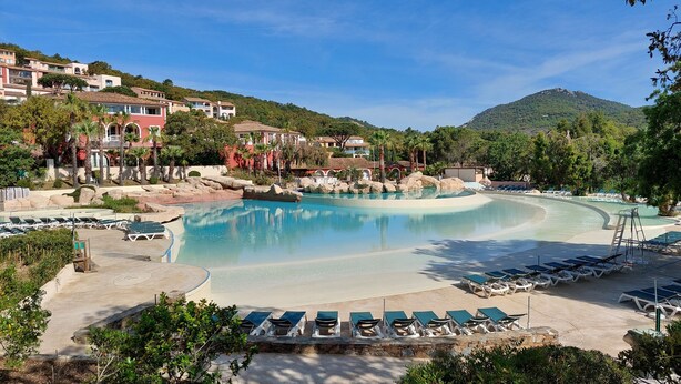 Un resort con una amplia piscina, sillas de descanso y montañas al fondo.