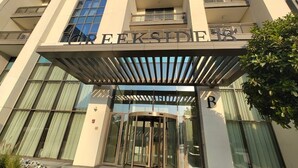 A modern building with a revolving door entrance, large windows, and a balcony on the upper floors. - Yogi - Elegant Apartment With Balcony Amidst Vibrant Area (Dubai)