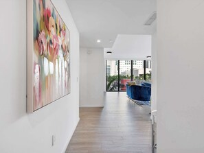 A modern interior with a wooden floor, a large abstract painting, and a view of the city through large windows.