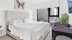 Une chambre moderne avec un grand lit, un téléviseur fixé au mur et une fenêtre donnant sur l’extérieur.