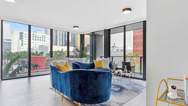 Une pièce spacieuse avec un canapé bleu, de grandes fenêtres et une vue sur la ville.