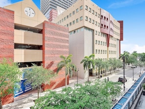 A multi-story building with a clock on the facade, a blue sign with white text, and a pedestrian walkway with trees. - X Lounge III-Modern Corner Residence (Miami)