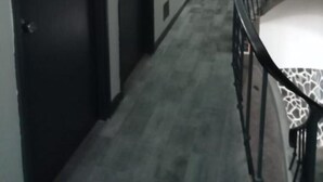 Un couloir doté d’un sol recouvert de moquette, d’un escalier avec une rampe en métal et d’une porte au-dessus de laquelle se trouve une lumière verte.