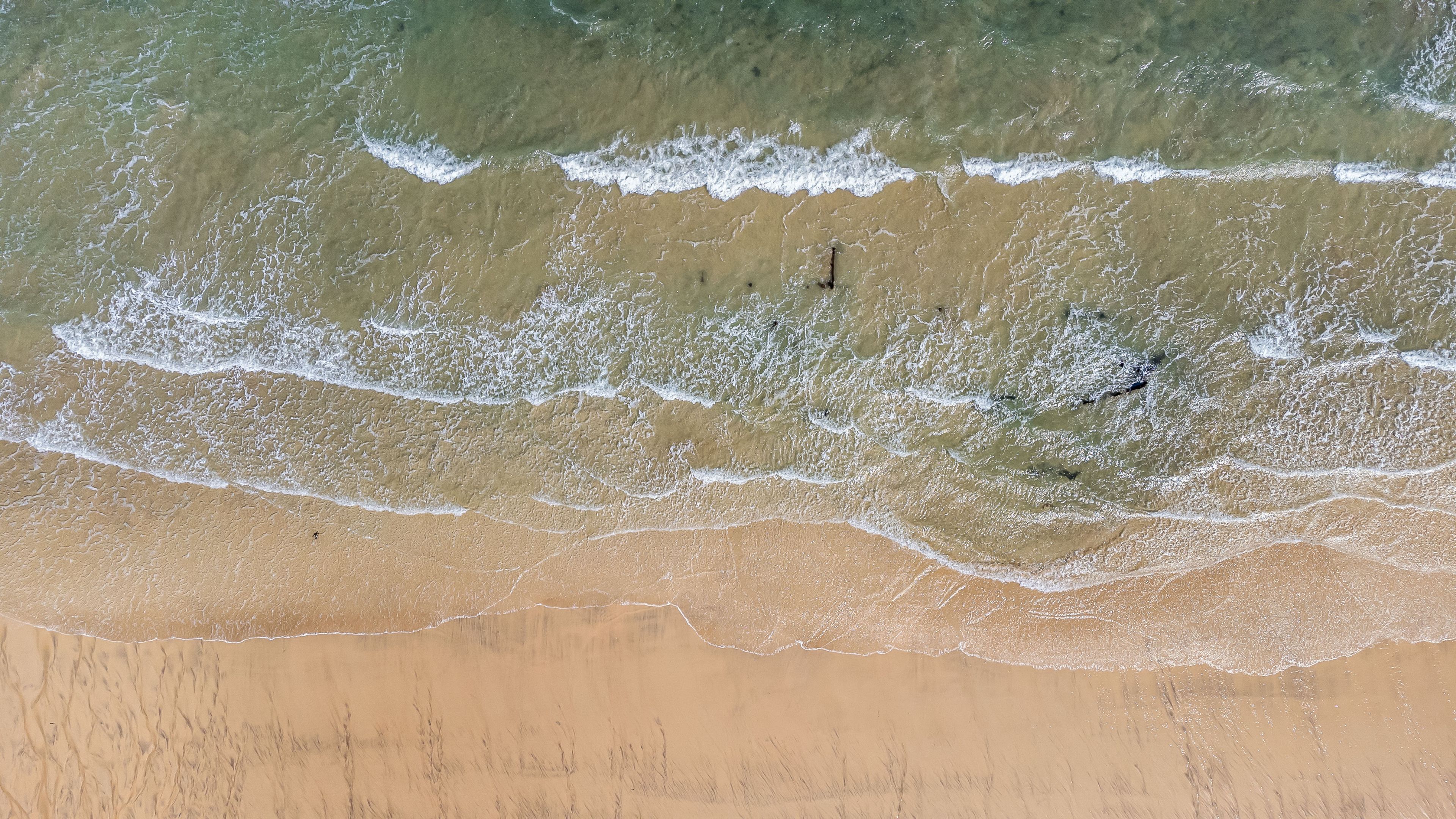 An aerial view of a beach with waves approaching the shore.