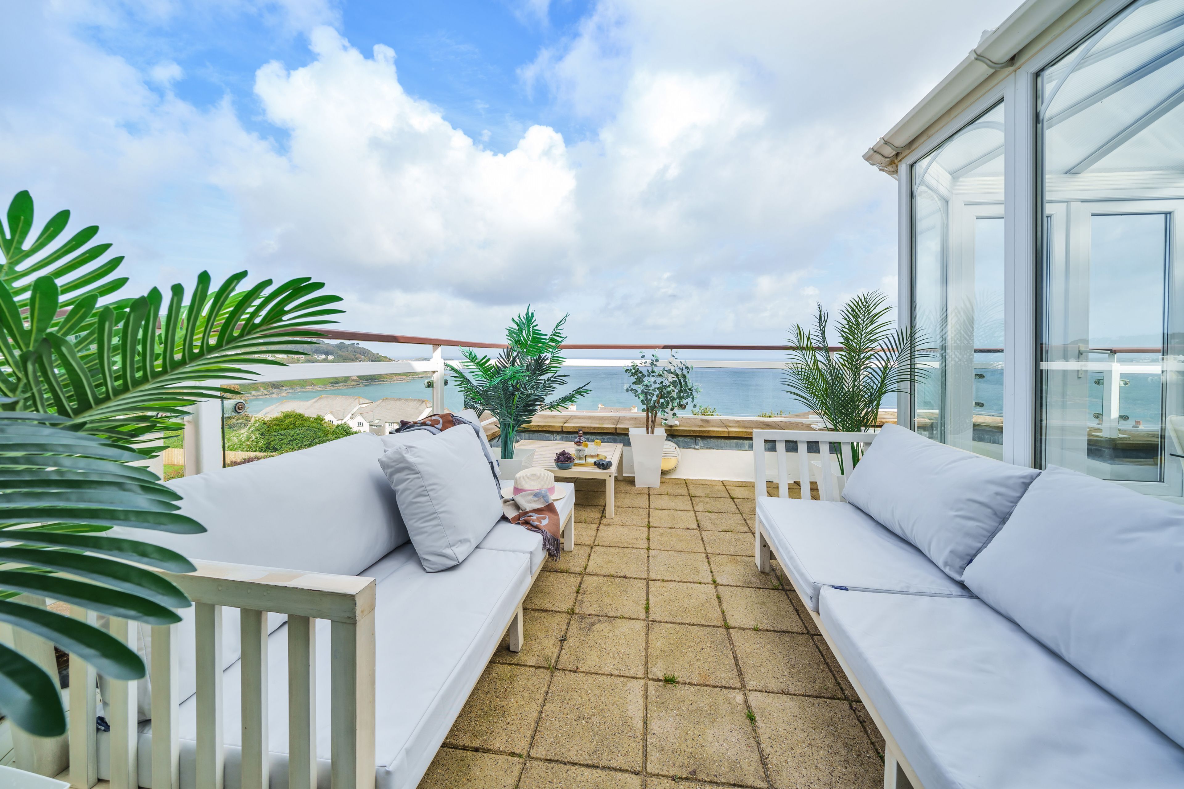 A balcony with white cushioned seating, a table, and potted plants.
