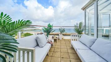 A balcony with white cushioned seating, a table, and potted plants.