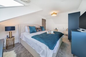 A modern bedroom with a bed, bedside table, lamp, and a desk with a computer.
