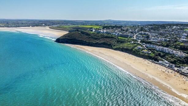 Vue aérienne d’une ville côtière avec une plage, des immeubles résidentiels et un ciel dégagé.