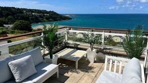 Une terrasse avec un canapé blanc, une petite table et une vue sur la mer et une côte lointaine.