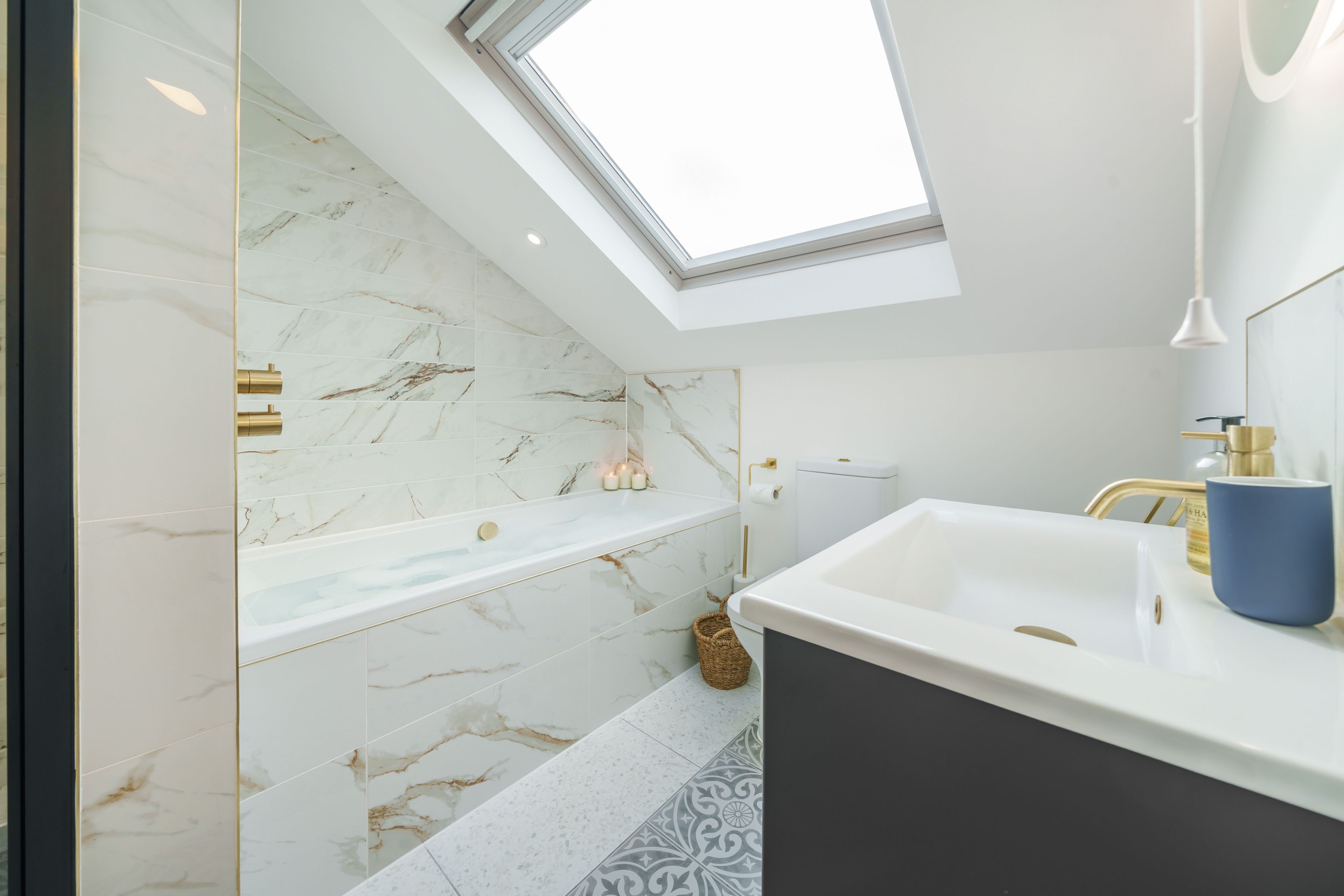 A modern bathroom with a skylight, a bathtub, a vanity with a sink, and a toilet.