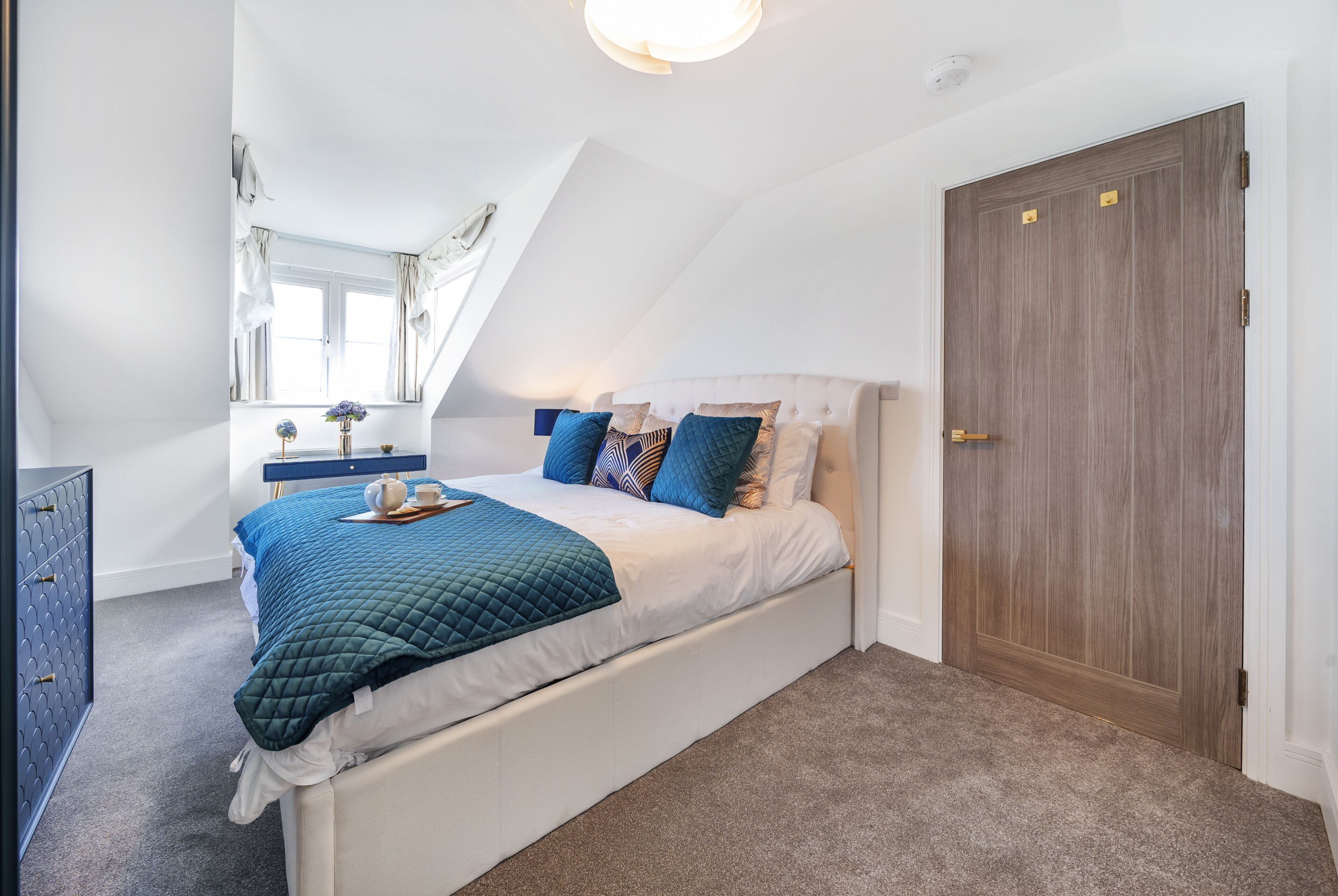 Ein Schlafzimmer mit Bett, Schminktisch, Fenster und Tür.