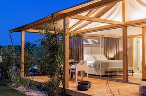 A modern tent-style accommodation with a bedroom, a seating area, and a view of the surrounding garden. - Infinito Resort (Carovigno)