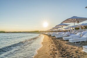 A beach with sun umbrellas and lounge chairs arranged along the shoreline. - Infinito Resort (Carovigno)