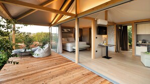 A modern, open-plan living space with a wooden deck, a sofa, a bed, and a dining area.