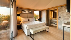 A modern bedroom with a large bed, a bench, a bedside table, and a bathroom visible through a sliding door.