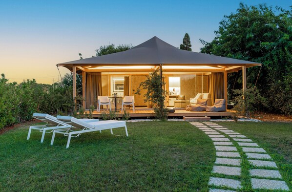 A modern outdoor lounge area with a covered seating area, a pathway leading to the entrance, and a well-maintained lawn. - Infinito Resort (Carovigno)