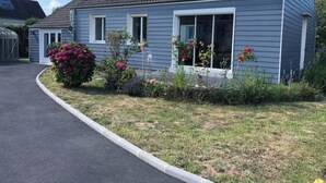 A single-story house with a dark blue exterior, a tiled roof, and a front yard with various plants and flowers.