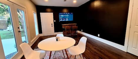 A dining area with a round table and four chairs, a ceiling fan, and a television on the wall.