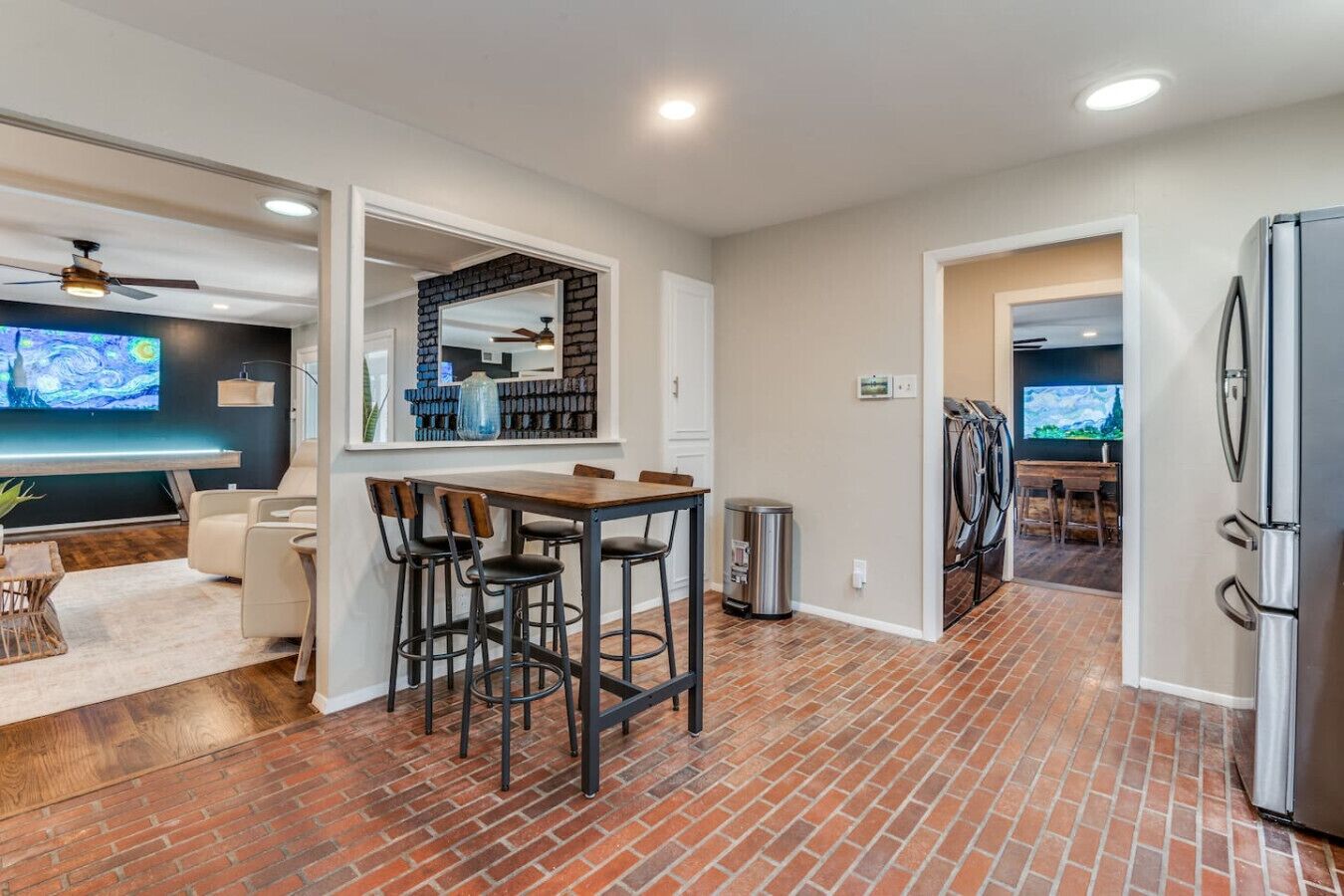 A modern kitchen with a brick floor, a dining area with bar stools, and a large mirror above the counter.