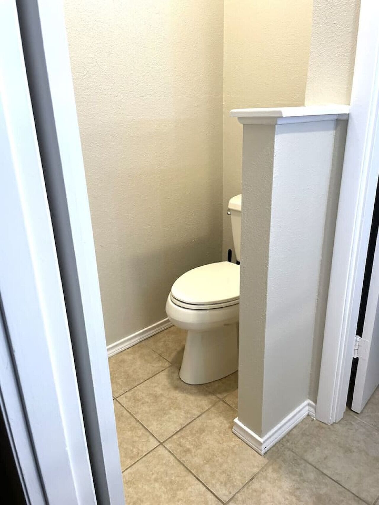 Ein kleines, sauberes Badezimmer mit Toilette, einem weißen Waschbecken auf Säule und beige gefliestem Boden.
