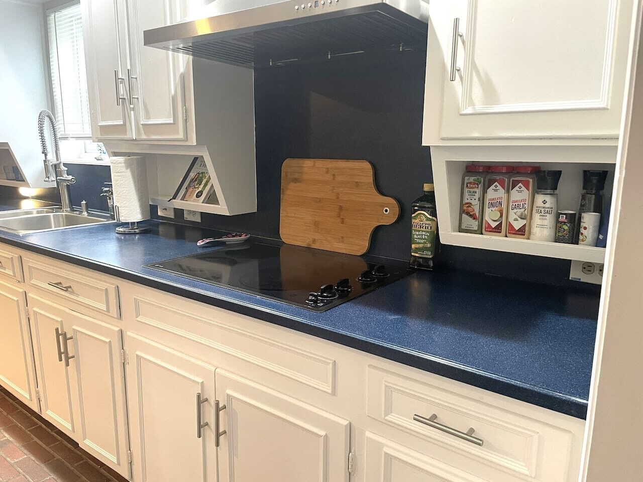 A kitchen with white cabinets, a blue countertop, a wooden cutting board, and various kitchen items.