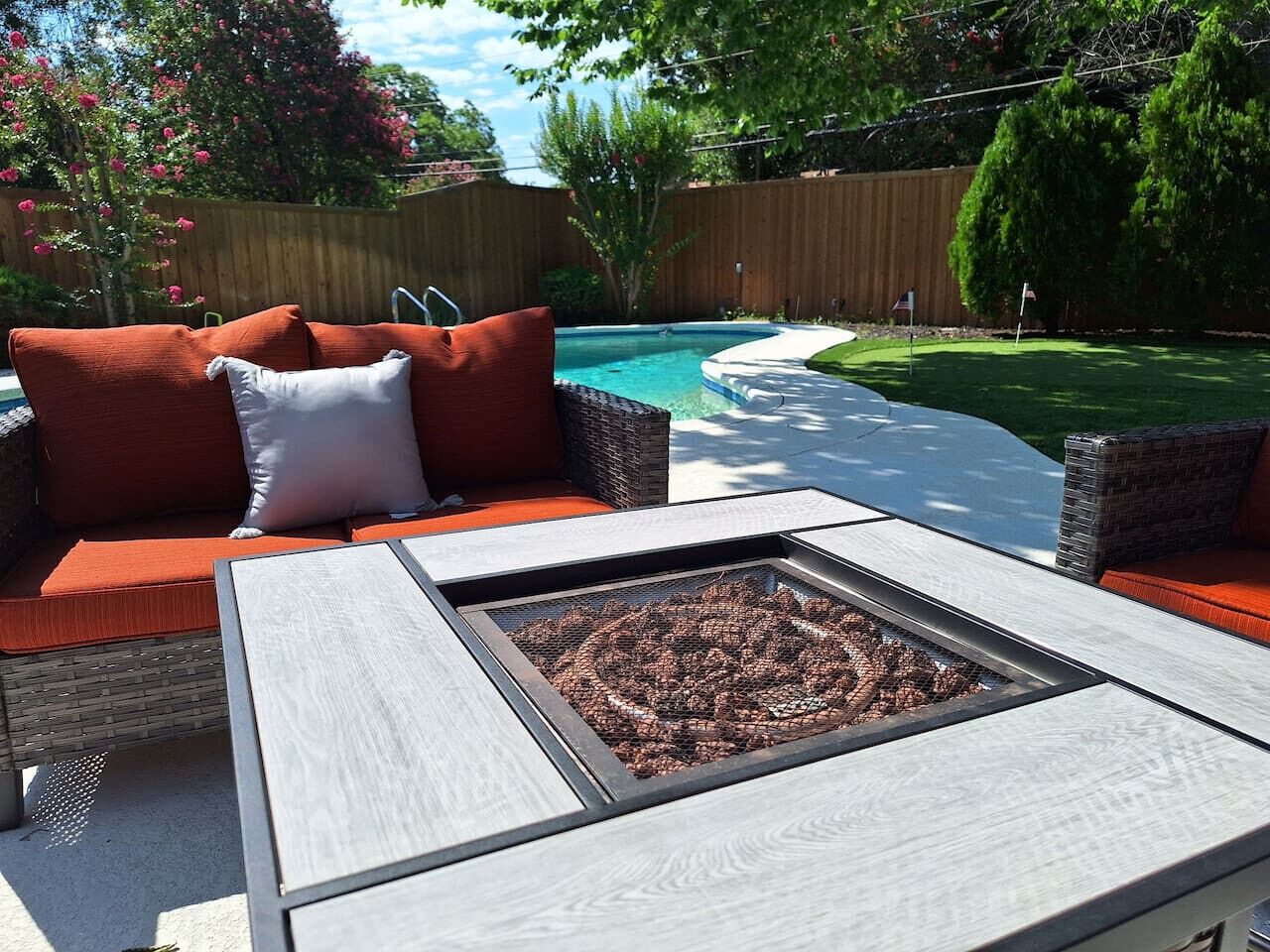 An outdoor patio with a fire pit, wicker furniture, and a pool in the background.