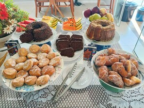 Una mesa con diversos postres y frutas, como pasteles de chocolate, rosquillas y frutas cortadas.