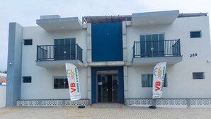 A modern building with a blue entrance, two balconies, and two banners with the logo "VB Hotéis e Eventos". - Pousada Ametista (Penha)