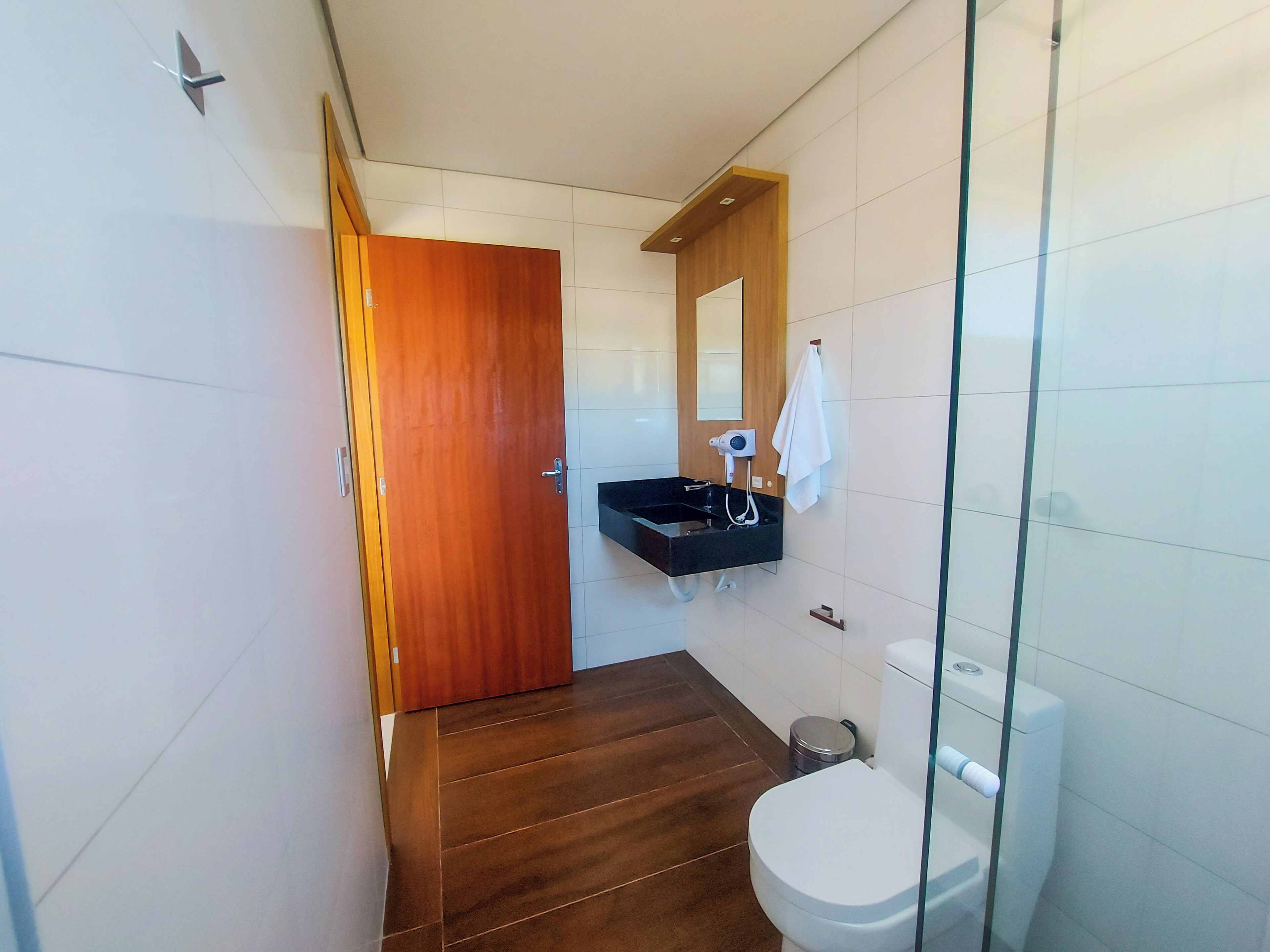 Un baño moderno con puerta de madera, lavabo negro, inodoro y mampara de vidrio.
