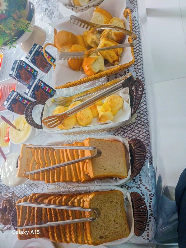 A buffet table with various food items, including bread, pastries, and chocolate-covered treats. - Pousada Ametista (Penha)